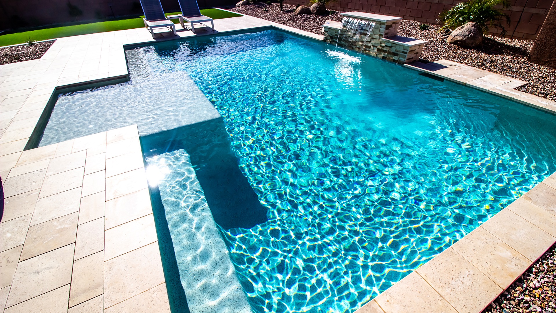 A sparkling blue swimming pool with two lounge chairs beside it, surrounded by a neatly landscaped patio and small garden.