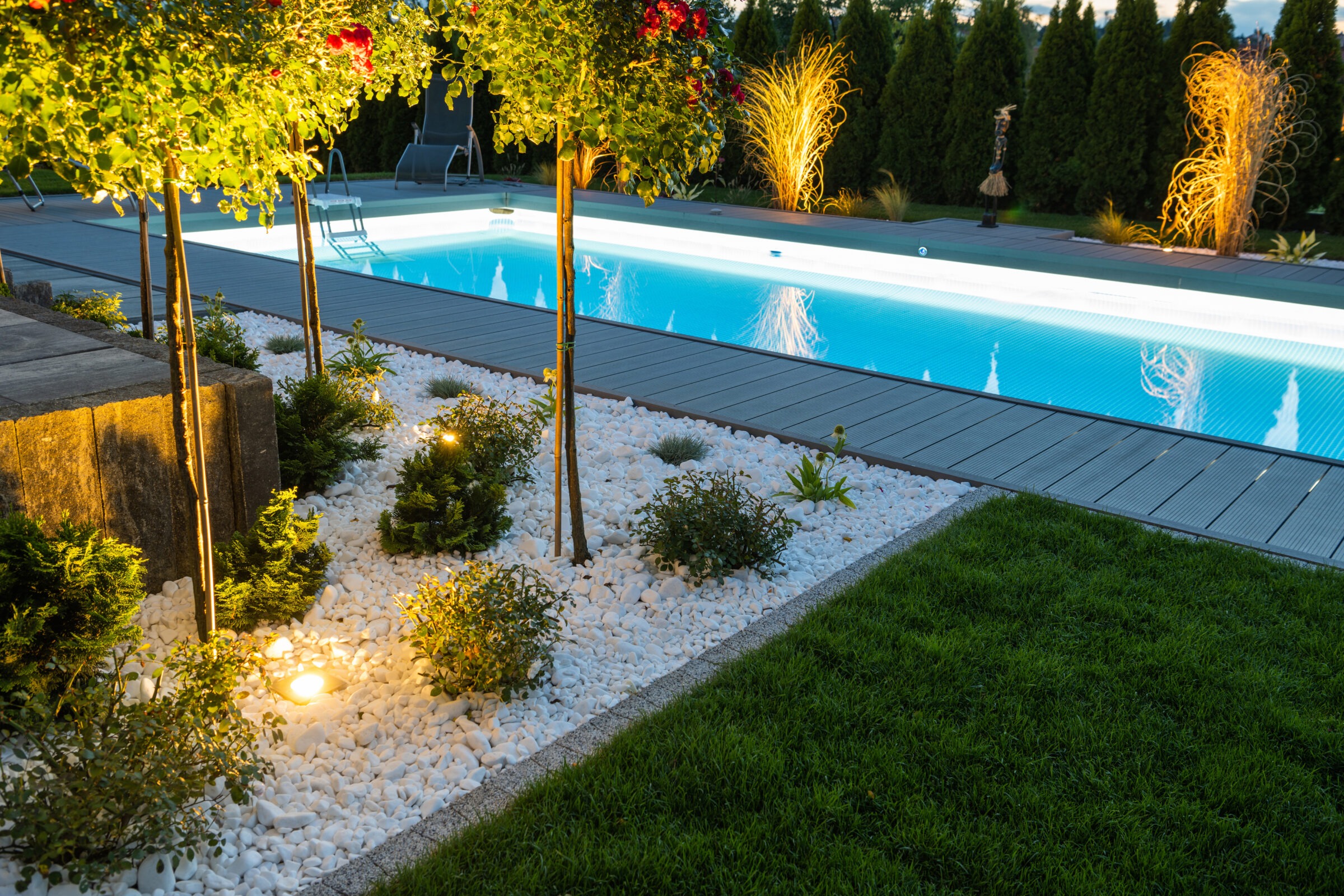 A lap pool at night with outdoor lighting and landscaping.