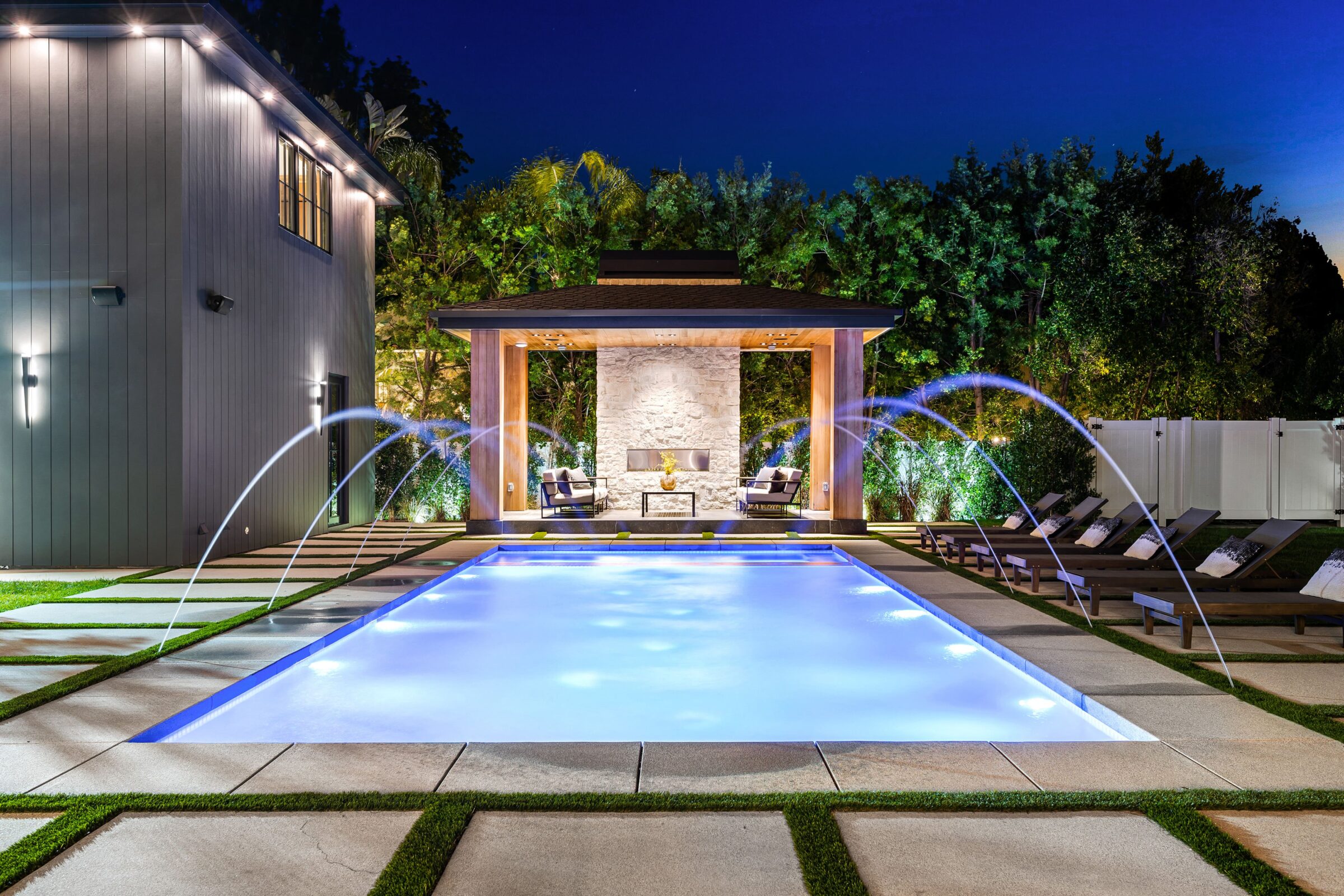 An inground pool with water features and modern lighting and pergola.